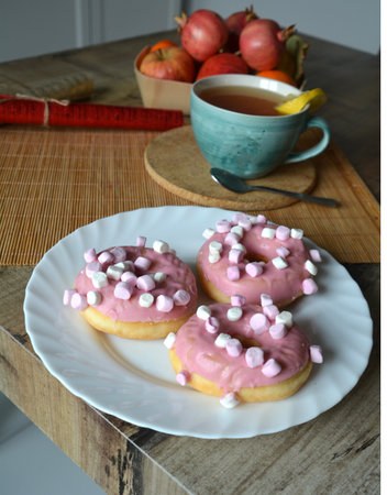Three donuts with pink icing on a wooden table. Sweet breakfast. Close-up.の写真素材