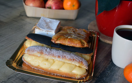 Eclairs, coffee and fruits on a wooden table. Selective focus.