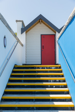 Swanage England  May 2015: Colourful red door with each one being numbered individually of white beach houses on a sunny day a view looking up the yellow stairs and a blue side wallのeditorial素材