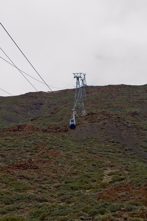 Looking up towards the cable car that pass through green and brown vegetation on the mountain on a bright sunny dayの写真素材
