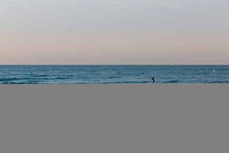 Golden sunset light of a silhouette of a surfer on his board moving towards the sea at the beach with sand  and no clouds in the sky in Europe with a blue summer skyの写真素材