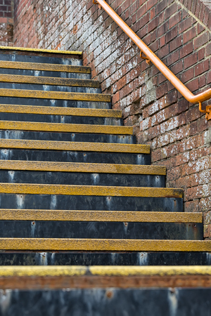 Detail of flight of stairs with yellow coloured safety threads and orange coloured stainless steel handrail, in a UK train stationの写真素材