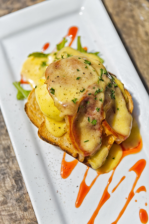 Brunch Idea; White crispy bread spread with holandaise sauce topped with bacon, lettuce and poached egg. Garnished with parsley, grilled sesame seed, salt and chili sauce.の写真素材