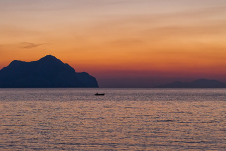 Small boat sunset silhouette is a fisherman's boat paddling along the water with a colorful purple and pink night sky in the backgroundの写真素材
