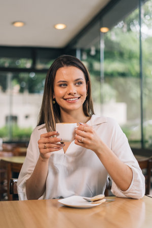 Vertical social media format photo of a Caucasian woman holding a cup of coffee. Concept of a person drinking coffee. Beautiful young woman sitting in a coffee shopの写真素材