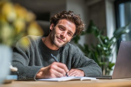Relaxed man writing in notebook in front of laptop in natural environment. Concept of inspiration, creativity, and remote work.の素材