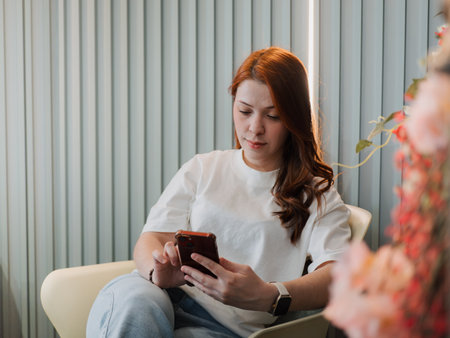 Young woman relaxes on a sofa while using her smartphone at home. Concept of mobile communication and everyday lifestyle.の写真素材