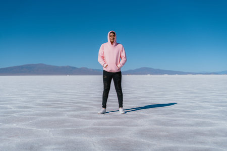 A man in a pink hoodie stands in the middle of a desert. The sky is clear and blue, and the...