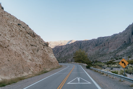 A road with a yellow sign. The road is empty and the sky is blue