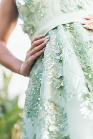 A woman is wearing a green dress with a floral pattern and sequins. She is standing in front of a...