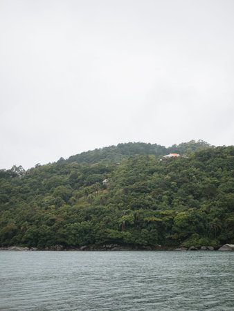 A mountain range with a house on top of it. The sky is cloudy and the water is calmの写真素材