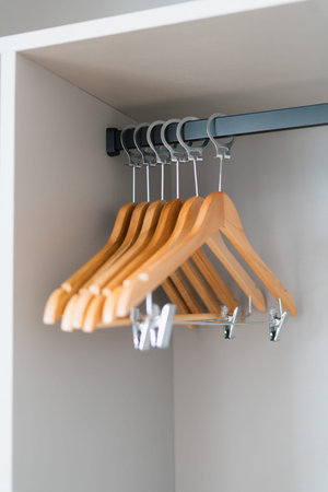 Wooden hangers rest on a black metal rod. Light gray walls surround the closet interior. Hangers are evenly aligned, natural wood finish. Ideal for home organization or fashion storage