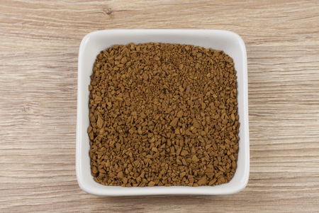 instant soluble coffee and coffee beans in a porcelain bowl on wooden backgroundの写真素材