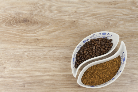 instant soluble coffee and coffee beans in a porcelain bowl on wooden backgroundの写真素材