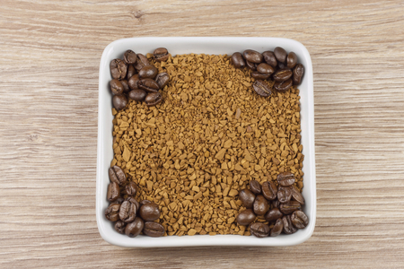instant soluble coffee and coffee beans in a porcelain bowl on wooden backgroundの写真素材