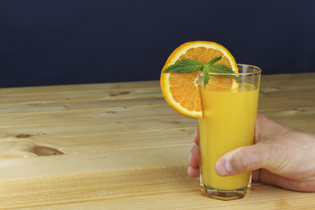 Man39s hand holding a glass of juice on a wooden table. Blue blurred background.の写真素材