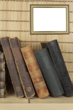 Front view of old books stacked on a shelf. Books without title and author. Old picture frame for your text.の写真素材