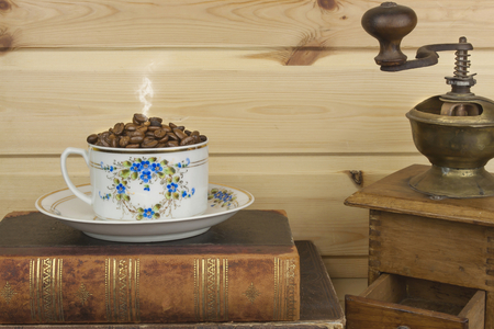 Mug coffee beans and old books are on the shelf. Resting comfort over coffee and reading. Background of wooden planksの写真素材