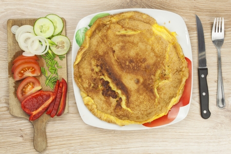 Scrambled egg omelet with vegetables on a wooden table. Preparation of fast food home.の写真素材
