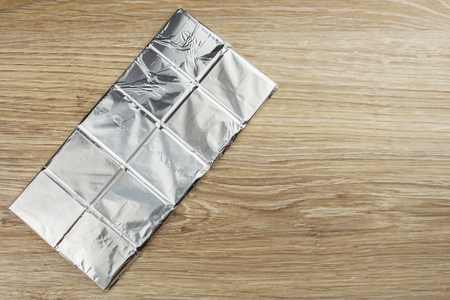 Chocolate wrapped in aluminum foil on a wooden board. Wrapped sweet treat.の写真素材