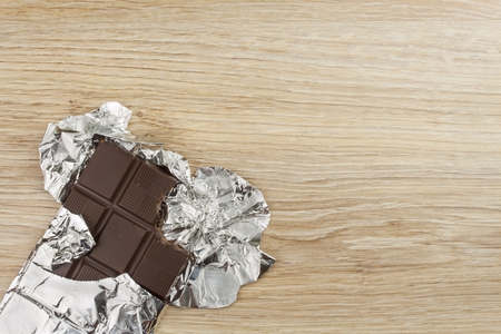Chocolate wrapped in aluminum foil on a wooden board. Wrapped sweet treat.の写真素材