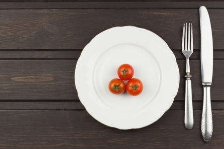 Very strict diet. Dietary vegetable diet. Tomatoes on a plate. Slimming diet. White plate with tomato on dark table.の写真素材