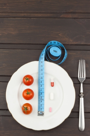 Diet and supplements on a wooden table. Strict diet meals. Slimming diet. Tomatoes and pills.の写真素材