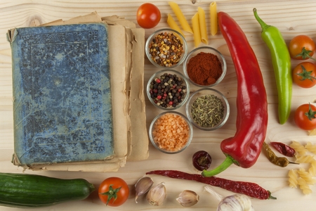 Old cookbook recipes on a wooden table. Cook healthy vegetable. Preparation of home diet food. Different kinds of vegetables.の写真素材