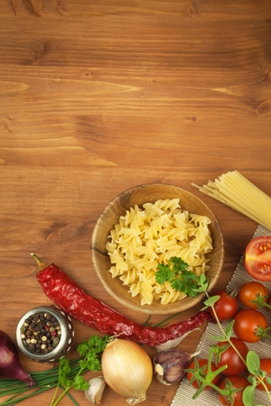 Raw pasta with tomatoes and parsley on a wooden background. Preparation diet food. Of The recipe for a simple dinner. Traditional pasta with vegetables.の写真素材