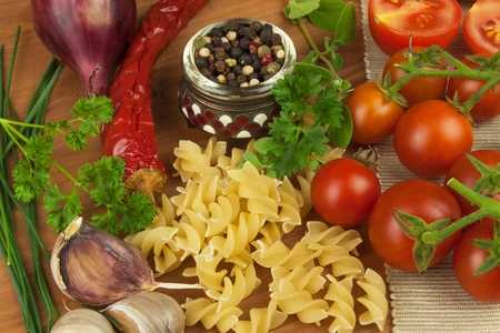 Raw pasta with tomatoes and parsley on a wooden background. Preparation diet food. Of The recipe for a simple dinner. Traditional pasta with vegetables.の写真素材