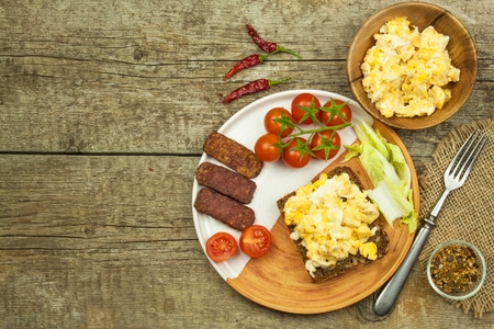 Scrambled eggs with bread and salami. Egg breakfast on a wooden table. Healthy food.の写真素材