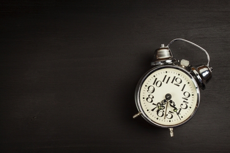 Retro metal alarm clock on a black wooden background. Open your eyes. Reveille to wake up. Place for...