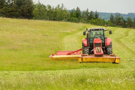 Work on an agricultural farm. A red tractor cuts a meadow