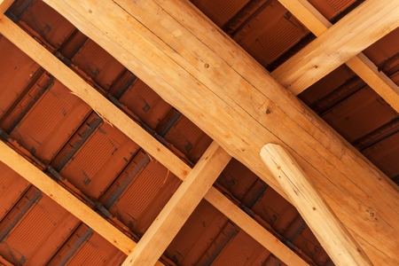 Wooden beams under a red brick roof during.  Detail of wooden roof structure