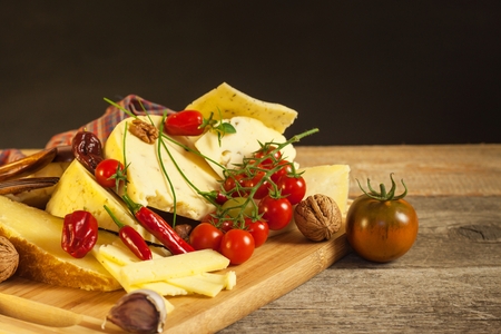 Sliced hard cheese on the kitchen board.  Production of cheeses on the farm. Spicy cheese, tomatoes, garlic, chilli, pepperの写真素材