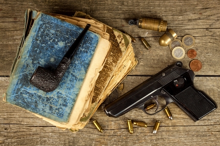 Gun and old book. Detective novel. Wooden tobacco pipe. Pistols and cartridges on the tableの写真素材