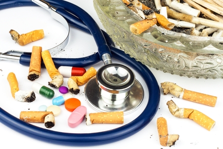 Cigarettes in a glass ashtray on a white background. Treatment of lung cancer.Stethoscope and medicationの写真素材