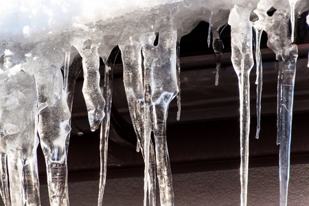 Icicles on a roof in a cold winter day. Icicles on house close up detail. A cold day. Climate changeの写真素材