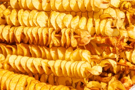 Spiral potatoes fried, on wooden sticks, spiral. Selling food at the market. Unhealthy fried food. Street food, and spiral fried potato on a stickの写真素材