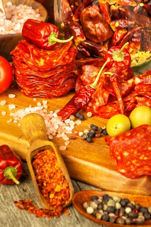 sausage or salami with chili pepper and herbs on wooden table. Spicy salami with chili. Unhealthy Fat Food.の写真素材