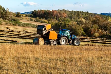 Blue tractor packs straw. Autumn work on the farm. Tractor on the field. Ecological agriculture.の写真素材
