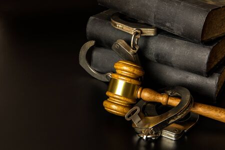 Police handcuffs and books of laws on black background. Wooden gavel and books on wooden table, law...