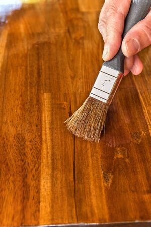 Applying protective oil on a wooden furniture. Varnishing the table top of acacia wood. Close-up view of a paintbrush. Housework.の写真素材