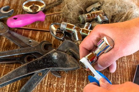 Plumber puts a sealing tape on the thread of the water valve, closeup. Plumbing tools on the table in the workshop. Repair of water pipes.の写真素材