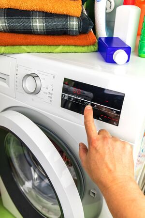 Close Up Of Man Choosing Cycle Program On Washing Machine. Adjusting wash settings on the control panel of washing machine. Smart home concept.の写真素材