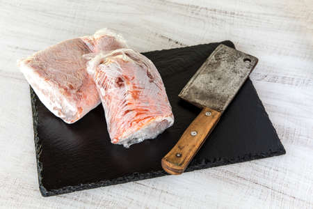 Frozen raw pork neck chops meat steak isolated on slate. Frozen uncooked slices of beef steaks,...