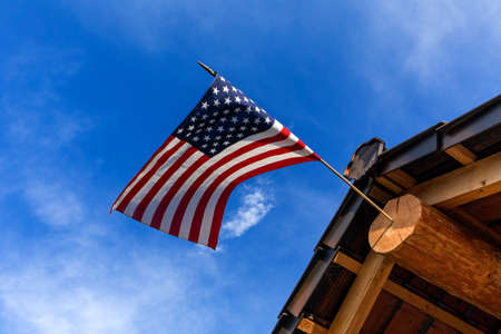 Log cabin roof & American Flag Against a Blue Sky. A red, white and blue American flag with stars and strips unfurled in the wind.の写真素材