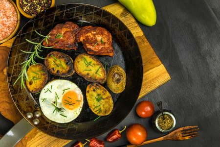 Closeup of fried pork chops in the frying pan on the stove decorated with rosemary. Pork neck with egg and potatoes. Fried meat.の写真素材