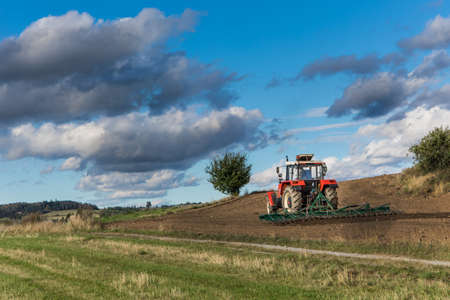 Red tractor cultivates the soil in the field with a cultivator after harvest. Autumn sunny day....