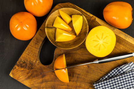 Ripe fresh persimmons on rustic background. Kaki fruit on wooden kitchen table. Slicing fruit on a kitchen board.の写真素材